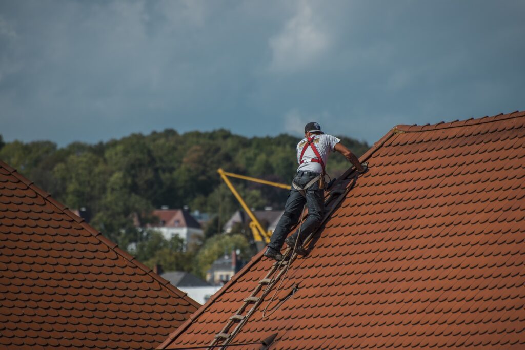 a man on a ladder fixing a roof Caption: Be sure to regularly clean your roof. It will hold out longer